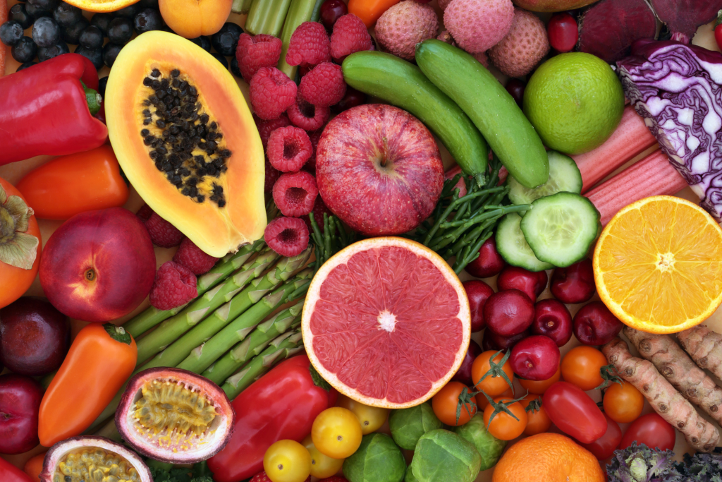 Flat lay of a variety of fruit and vegetables, including apples, raspberries, asparagus, bell pepper, blueberries, orange and tomatoes